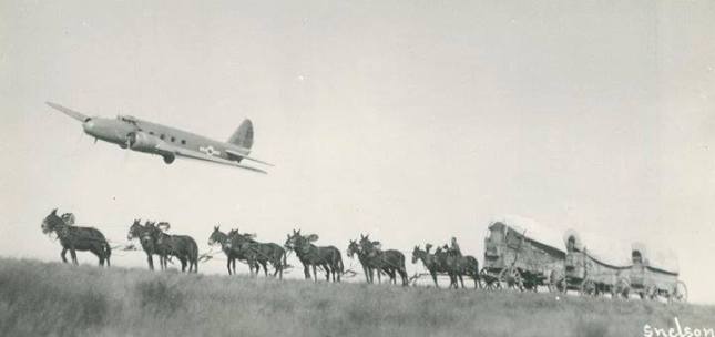 Photo of airplane flying over a wagon train