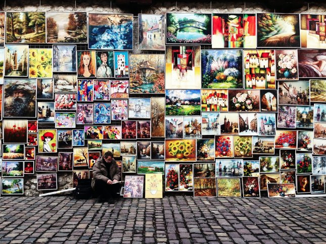 Photo of a man sitting in front of a wall of paintings