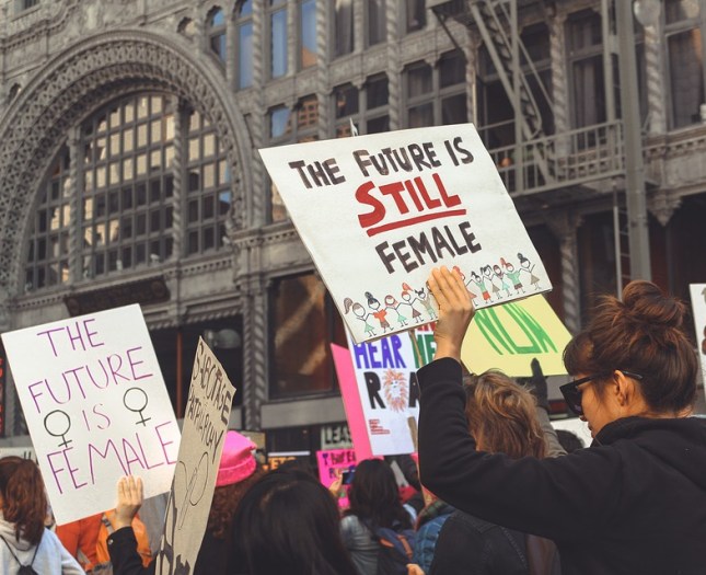 Photo of protest march with sign reading "The Future is Still Female"